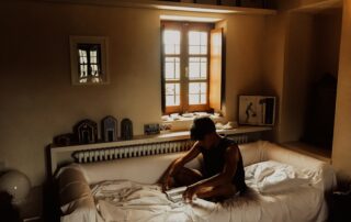 man sitting on bed beside opened window